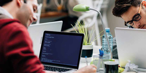 2 Personen sitzen vor einem Notebook und schreiben etwas auf ein Blatt Papier