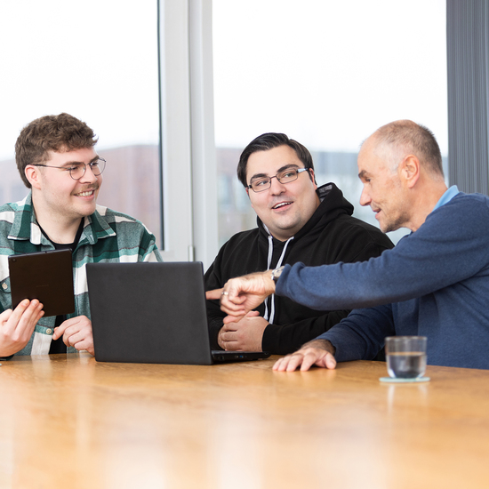 Beratungssituation mit drei Personen vor einem Notebook in Konferenzraum 