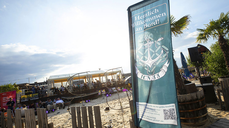 Strandbar mit Gästen und einem Banner zur Feier des 33. Jubiläums von ICN bei Herrn Walter 